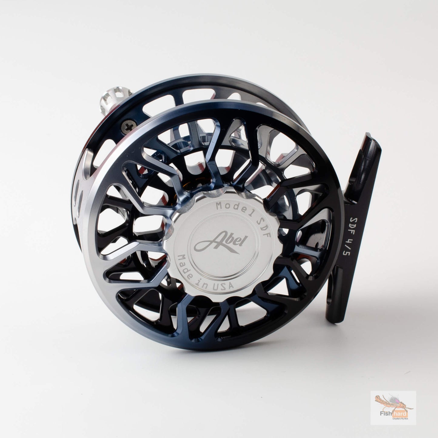 A close-up studio shot of a fly fishing reel on a light gray background. The reel features a dark blue and black metallic body with a polished silver center cap engraved with the brand name 'Abel'.