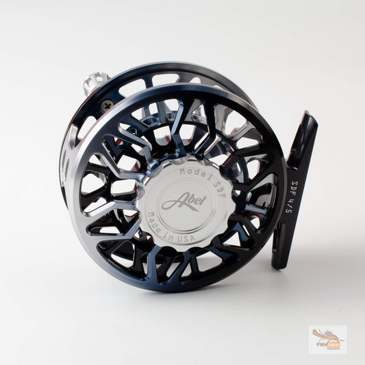 A close-up studio shot of a fly fishing reel on a light gray background. The reel features a dark blue and black metallic body with a polished silver center cap engraved with the brand name 'Abel'.