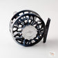 A close-up studio shot of a fly fishing reel on a light gray background. The reel features a dark blue and black metallic body with a polished silver center cap engraved with the brand name 'Abel'.