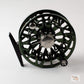 A dark green and black fly fishing reel with a silver metal center cap, shown on a light gray background.