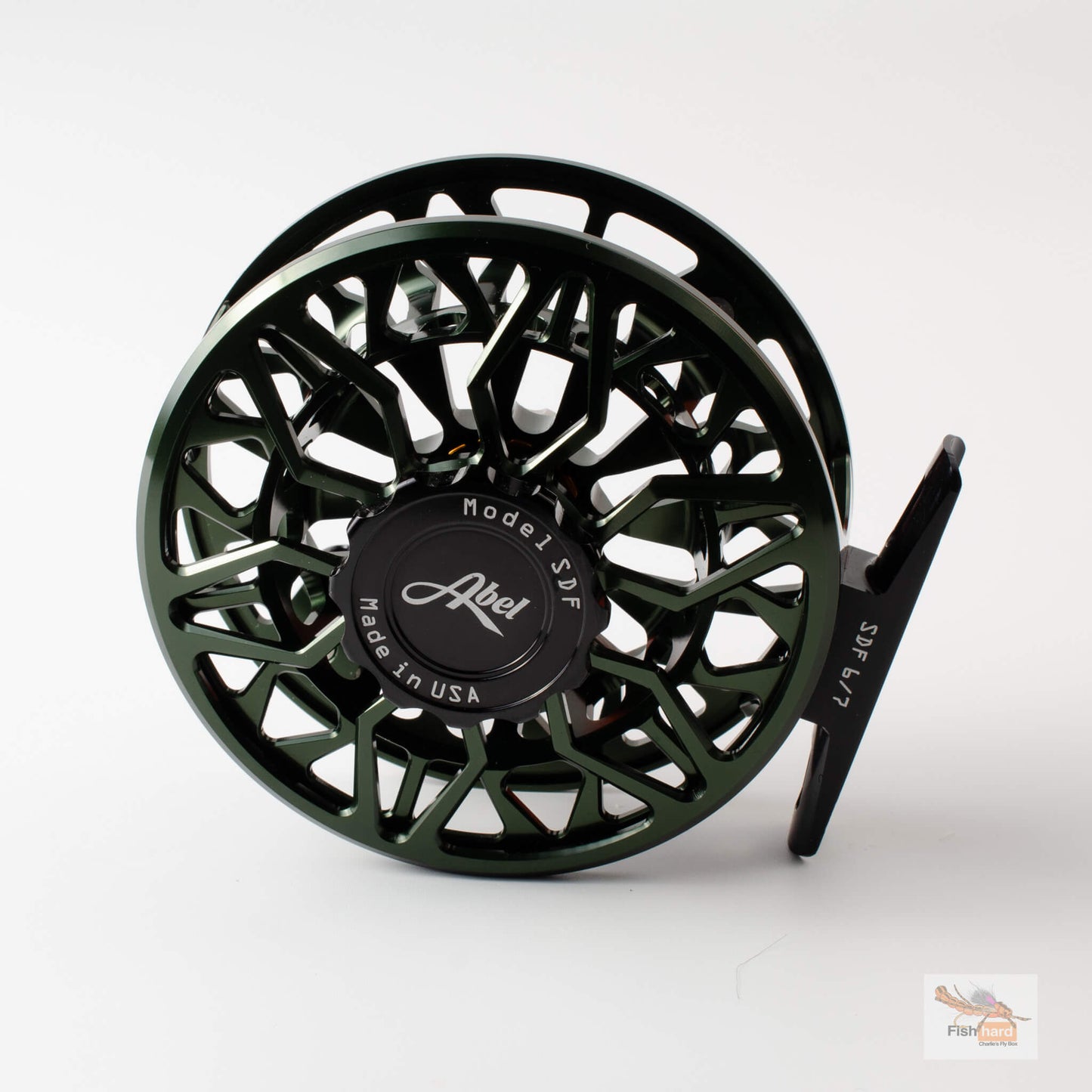 A dark green and black Abel fly fishing reel with a complex cutout frame design, shown on a clean white background with a subtle reflection.