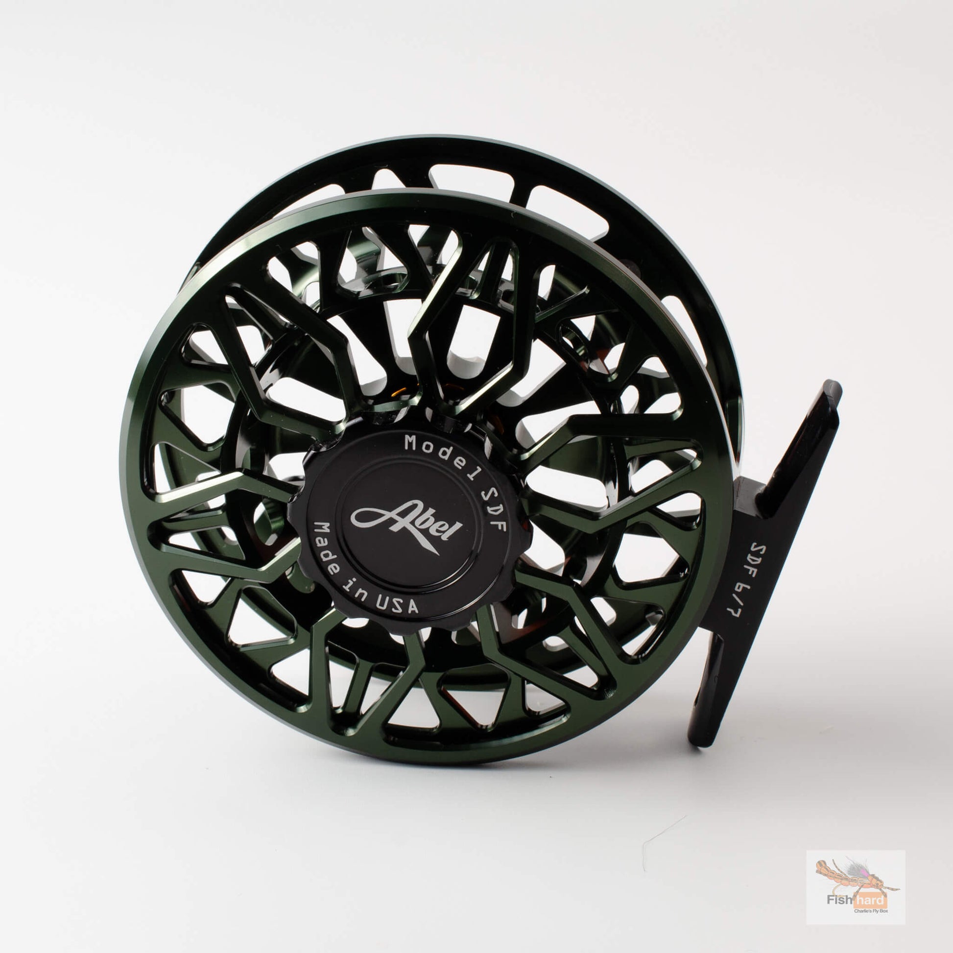 A dark green and black Abel fly fishing reel with a complex cutout frame design, shown on a clean white background with a subtle reflection.